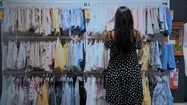 ショッピング セールシーズン 衣料品店で 若いブルネットの女性が 買いたいパジャマ ホームウェア 下着を選びます スーパーマーケットかモールの下着の部門 お客様は服を着ている — ストック動画