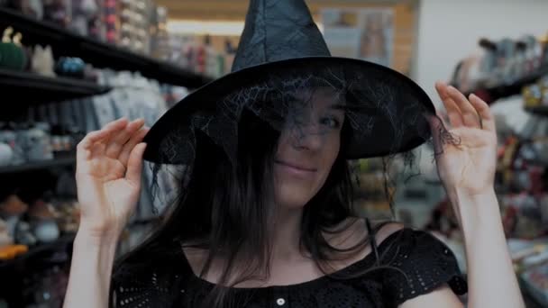 万圣节女巫万圣节派对女巫服装 购买万圣节饰物 在商店里 一个漂亮的黑发女人正试着戴着一顶黑女巫帽参加万圣节派对 — 图库视频影像