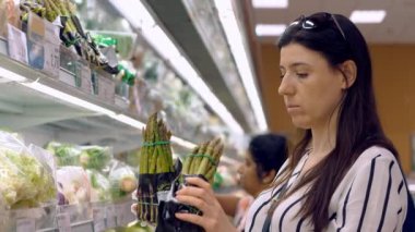 Asparagus officinalis. packaged asparagus, on shelves in a supermarket. a woman chooses asparagus to buy in a supermarket, in the grocery department, in the vegetable shop.