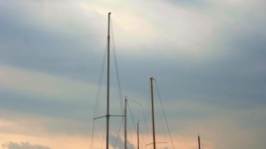 Yatçılık. Yelkenli yatların direkleri. Deniz manzarası. Gün batımı. Yelkenli yatların direkleri rüzgarda sallanıyor, gökyüzüne karşı, günbatımında. Hava bulutlu. Sinematik çerçeve 