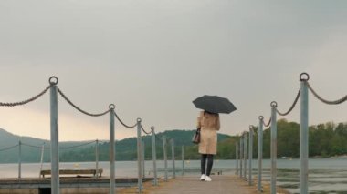 Dağlarda bir göl. Yağmurluk giymiş ve siyah şemsiyeli bir kadın gün batımında gölün ve dağların manzarasının tadını çıkararak rıhtımda tek başına yürüyor. Ilık bahar akşamı. Sakin ve yatıştırıcı.