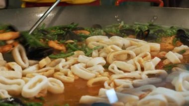 Deniz ürünleri pişirmek. Yakın plan. Yeşil bezelye, fasulye, sarımsak, baharat ve domates soslu büyük bir tavada midye, karides ve kalamar kızartmak.