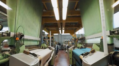 Kumaş üretim fabrikası. Dokuma tezgahı. Tekstil fabrikasının atölyesinde çalışan birçok otomatik dokuma makinesi. Dokuma. 
