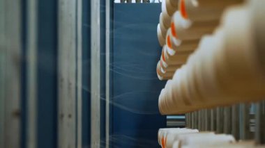 İplik makaraları. Yakın plan. Bir sürü iplik makarası olan raflar. Endüstriyel tekstil fabrikasının atölyesi. Boyama için iplikleri hazırlama süreci, istenen kumaşların daha fazla üretimi için