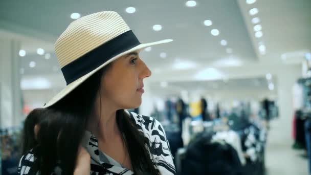 買い物をする ポートレート 女性は新しい服を選ぶ 彼女は夏の帽子を 大きなブリムで試してる 新しい服を選ぶこと ワードローブを更新すること 購入する 衣料品店について カジュアルな服のためのショップ — ストック動画