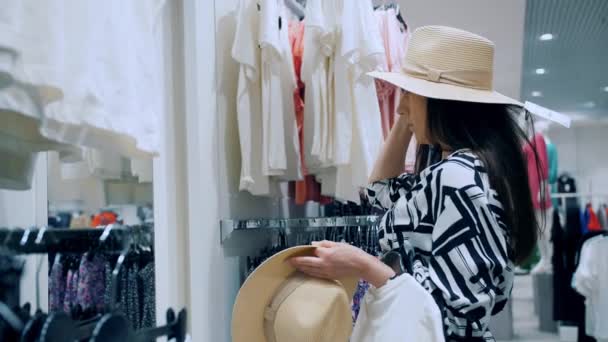 Fazer Compras Mulher Escolhe Roupas Novas Ela Tenta Chapéu Verão — Vídeo de Stock