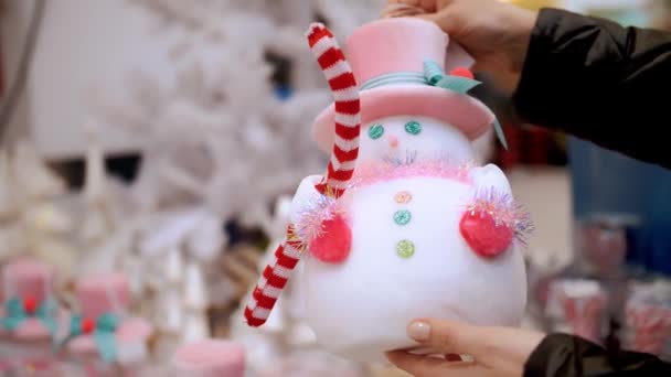 クリスマス スノーマンのおもちゃ クリスマスの装飾 アクセサリー ショッピング クローズアップ クリスマスの装飾を手に持っている女性 店舗での冬季休暇のためのお祝いのアクセサリーの選択と購入 — ストック動画