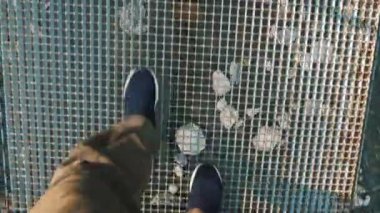 Asma köprü. Yakın plan. Spor ayakkabılı bir turistin bacakları bir dağ nehrinin üzerinde, boş metal asma köprü boyunca yürüyor. Yaz günü. seyahat ve macera