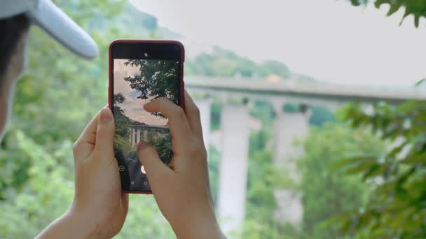 クローズアップ 夏の間 公園の女の子は 彼女の携帯電話に美しい風景を撮影しました バックグラウンドの車とアルプスのための橋 高品質の4K映像 — ストック動画