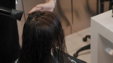Stüdyodaki kuaför kadın müşterinin saçını saç kurutma makinesiyle kurutuyor. Profesyonel kuaför kuaförde saç stili yaratır. Sahibi müşterinin saçlarıyla ilgilenir. Yüksek kalite 4k görüntü
