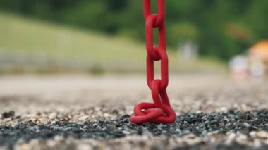  Sallanan kırmızı metal zincir. Yakın plan. Kırmızı zincir yoldaki asfaltın üzerinde asılı. Zincir halkaları. Bulanık arkaplan.