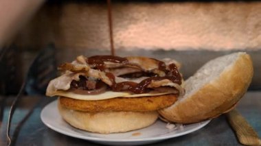 Hamburger pişirmek. Yakın plan. Şef hamburgere lezzetli malzemeler ekler, taze salatalık, domates, sulu, peynirli ızgara biftek ve üstüne kızarmış yumurta gibi. fast food. Yüksek kalite 4k görüntü