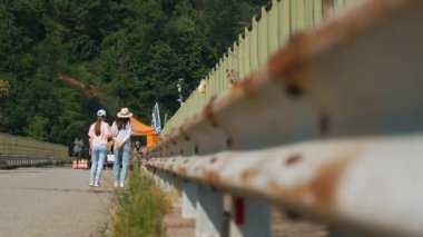 Yolda yürüyen iki kız. Alpler 'de yaz günü. Arabalar için yol bariyerleri kötü durumda. Rusty, tamire ihtiyacım var. Yüksek kalite 4k görüntü