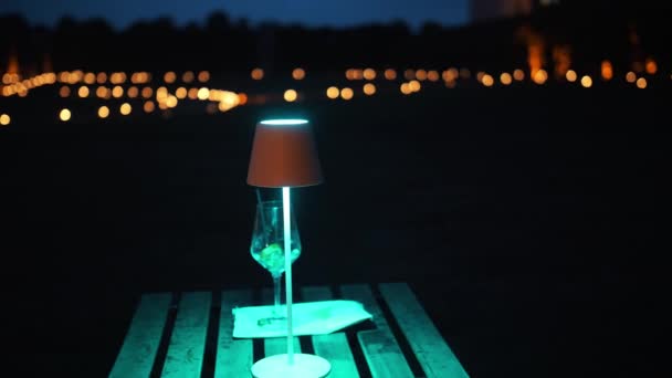 ライトランプ付きの空のテーブル 夕方の雨 テーブルの上には 消費されたカクテルの空のグラス 地面にたくさんのろうそくが付いている輝かしい背景 高品質の4K映像 — ストック動画
