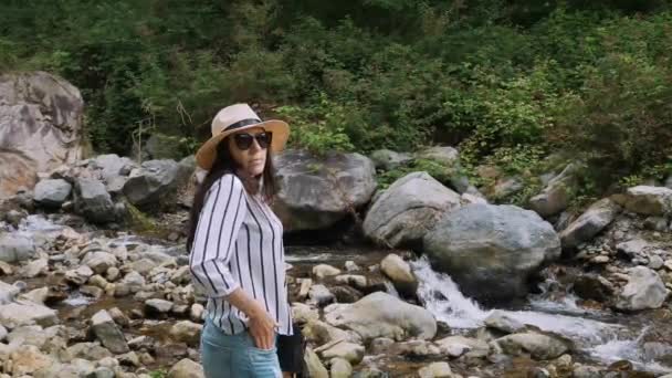 一个戴帽子的女孩的画像 夏天在阿尔卑斯山里散步 这个背负着一条山河的女孩面带微笑 充满了快乐和欢乐 高质量的4K镜头 — 图库视频影像