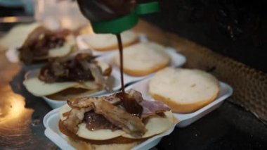 Hamburger pişirmek. Yakın plan. Şef hamburgere lezzetli malzemeler ekler, taze salatalık, domates, sulu, peynirli ızgara biftek ve üstüne kızarmış yumurta gibi. fast food. Yüksek kalite 4k görüntü