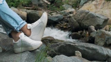 Kızlar bacaklarını bir dağ nehrinin arka planına yasladı. Dağlarda turizm ve dinlenme. Yaz tatili. Yüksek kalite 4k görüntü