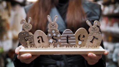 Paskalya indirimi. Yakın plan. Paskalya bayramında geleneksel paskalya tavşanları ve yumurtalarla süslenmiş ahşap bir süsleme tutan kadın elleri. Paskalya süslerinin alışverişi ve dükkandaki ev için hediyeler.