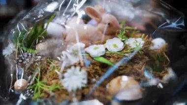 Paskalya panayırı. Yakın plan. Paskalya süslerini tutan kadın elleri. Paskalya kompozisyonu, saydam ambalajda bir tavşan ve yumurta. Katolik Paskalyası için geleneksel Avrupa dekorasyonu 