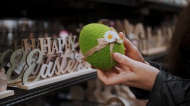 Paskalya panayırı. Yakın plan. Kadın elleri komik yeşil bir Paskalya yumurtası heykelciği tutuyor. Geleneksel Avrupa paskalya dekorasyonu ve dekorasyonları. Paskalya alışverişi, mağazada vitrin.. 