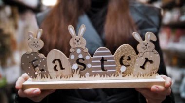 Paskalya indirimi. Yakın plan. Paskalya bayramında geleneksel paskalya tavşanları ve yumurtalarla süslenmiş ahşap bir süsleme tutan kadın elleri. Paskalya süslerinin alışverişi ve dükkandaki ev için hediyeler.