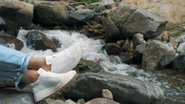 Kızlar bacaklarını bir dağ nehrinin arka planına yasladı. Dağlarda turizm ve dinlenme. Yaz tatili. Yüksek kalite 4k görüntü