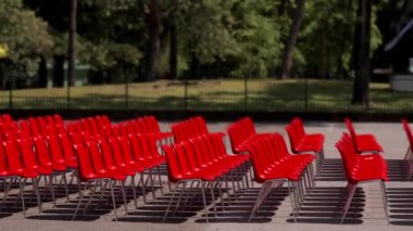 Simetrik sıra halinde kırmızı sandalyeler dışarıda düzgünce dizilmiş bir park etkinliği için seyirci bekliyorlar. Arka plandaki yemyeşil ağaçlar çarpıcı kırmızı sandalyelerle canlı bir tezat oluşturuyor.