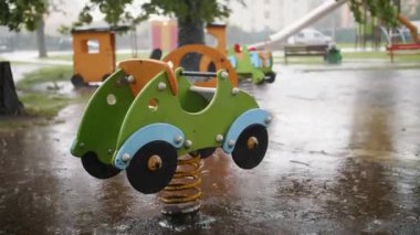 Bir çocuk oyun parkında yağmura bulanmış araba şeklindeki bir bahar binicisinin canlı fotoğrafı kasvetli ama renkli bir günü resmediyor.