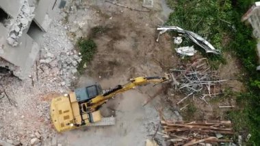 Kırık yapılar ve dağınık molozlarla çevrili sarı bir kazıcının aktif olarak enkazı temizlediğini gösteren bir yıkım alanının yukarıdan görüntüsü.