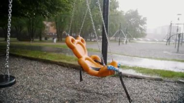 Islak, su lekeli bir salıncakla dolu bir oyun alanı. Yağmur yağarken, şehir parkında yalnızlık ve sessizlik hissi uyandırıyor.