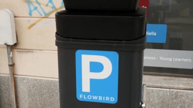 BIELLA, İtalya, 25 Nisan 2024: Akış Kuşu 'ndan güneş enerjili bir parkmetreye yakın çekim, arka planda şehir yaşamı unsurları, çevre dostu kentsel ulaşım çözümleri