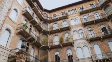 Zarif bir şekilde yaşlanan balkonların, kemerli pencerelerin ve temiz bir gökyüzüne karşı döşenmiş karmaşık tuğla işçiliğinin olduğu bir binanın ayrıntılı görüntüsü