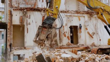 BIELLA, İtalya, 25 Nisan 2024: Güçlü bir yıkım kazıcısı eski bir binayı yıkıyor, kentsel yenileme ve inşaat sürecini gösteriyor. Makine karşı çalışırken enkaz etrafa saçılıyor.