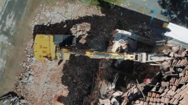 Havadan bakıldığında, yıkılan bir binanın ortasında, kentsel yenileme ve inşaat sürecini gösteren bir kazıcı görülüyor. Ağır makineleri çevreleyen enkaz şehrin dinamik doğasını yakalıyor.