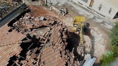 Bir kazıcı, yıkım alanındaki yıkıntıları temizlemeye çalışıyor. Etrafı tuğlalarla ve inşaat atıklarıyla çevrili. Kentsel yenilenme çalışmaları.