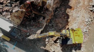 Şehir binalarının yıkılması, endüstriyel parçalanma ve kentsel yenilenme süreçleri sırasında molozların ortasındaki sarı kazıcının yüksek açılı görüntüsü.