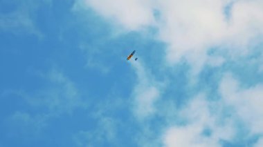 Canlı bir planör, açık havada özgürlük ve macera duygusunu yansıtan tüylü beyaz bulutlarla kaplı berrak, parlak mavi bir gökyüzüne doğru uçar.