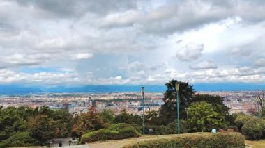 Uçsuz bucaksız bir şehir manzarasına bakan bu resim yoğun bir şekilde tıklım tıklım dolu şehir binalarının yoğun bulutlarla dolu dramatik bir gökyüzünün altında birbirine karışmış yeşil alanlar arasında bir kontrasttır.