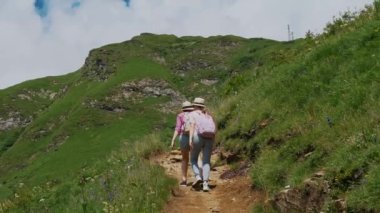 Bir aile, serpilen kır çiçekleri ve manzaralı bir dağ zeminiyle çevrili canlı yeşil bir vadide yaz etkinliklerinin güzelliğini vurgulayan huzurlu bir yürüyüşün tadını çıkarıyor.