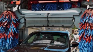 Otomatik araba kurulanıyor. Otomatik oto yıkamadan geçen bir arabanın yakın plan görüntüsü, canlı mavi ve kırmızı fırçalar, verimli bir temizlik sürecini gösteriyor