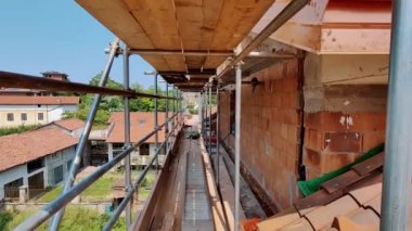 Açık bir gökyüzü altındaki yapılar arasında dar bir geçitten aşağıya doğru uzanan, iskele, tamamlanmamış tuğla binalar içeren kentsel bir inşaat alanına ayrıntılı bir bakış.