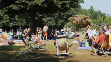 Yaz boyunca bir şehir parkında canlı bir sahne çeşitli insanların dinlendiği, sohbetlere daldığı ve güneşli bir günde güneşli havanın tadını çıkardığı.