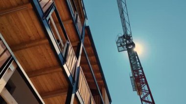 Kereste çerçeveli bir binanın parlak güneş ışığı altında yükselen bir vinçle çarpıcı kontrastı, kentsel gelişim ve mimari teknikler sergiliyor.
