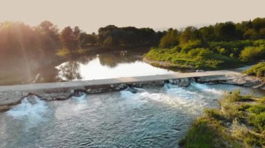 Şelaleden bir Weir 'ın hava görüntüsü. Küçük Barajı olan Huzurlu Nehir, Yeşillik ile çevrili. Gün batımında nehrin üzerindeki beton köprü. Yüksek kalite 4k görüntü