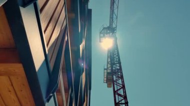 Şehir gelişimini ve mimari gelişimi tasvir eden modern ahşap bir binanın yanındaki yüksek inşaat vincinin üzerinde parlak güneş ışığı parlıyor.