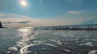 Gün batımında sakin bir plaj sahnesinde hafif dalgalar, titreyen su ve bir yaz akşamı boyunca sakin ve sakin bir şekilde hareket eden engin, bulutlu bir gökyüzü yer alır.