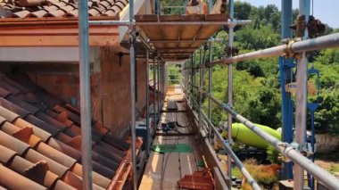 Konut binasında çatı tamiri, geniş yapı iskeleleri, inşaat aletleri ve açık bir gökyüzünün altında çatı malzemeleri. Yerleşim Katı Tiling 'in İlerlemesi.