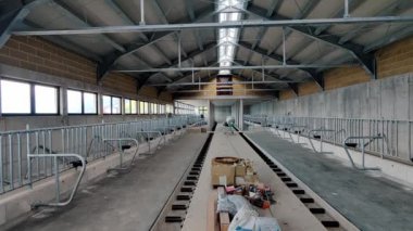 İnşaat halindeki bir mandıranın geniş açılı görüntüsü, temiz ve modern sığır ahırları, beslenme hattı ve pencereli endüstriyel bir çatısı var.
