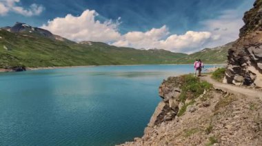 Açık mavi bir gökyüzünün altında, dağlık bir gölün yanında nefes kesici bir dağ yolu boyunca birkaç yürüyüş. Açık hava macerasının ve doğa keşiflerinin özü.