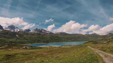 Görkemli dağlara ve yemyeşil çayırlara karşı kurulmuş sakin bir alp gölünün sükunetini yakalayın. Huzur dolu arka planlar için ideal.
